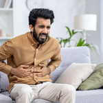An Indian man suffered with indigestion pain problem sitting on a sofa