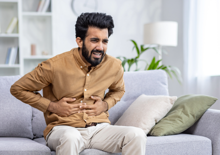 An Indian man suffered with indigestion pain problem sitting on a sofa