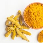 Haldi roots and powder in a spoon and bowl