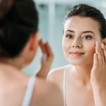 beautiful smiling girl touching face and looking at mirror in ba