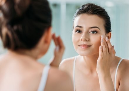 beautiful smiling girl touching face and looking at mirror in ba